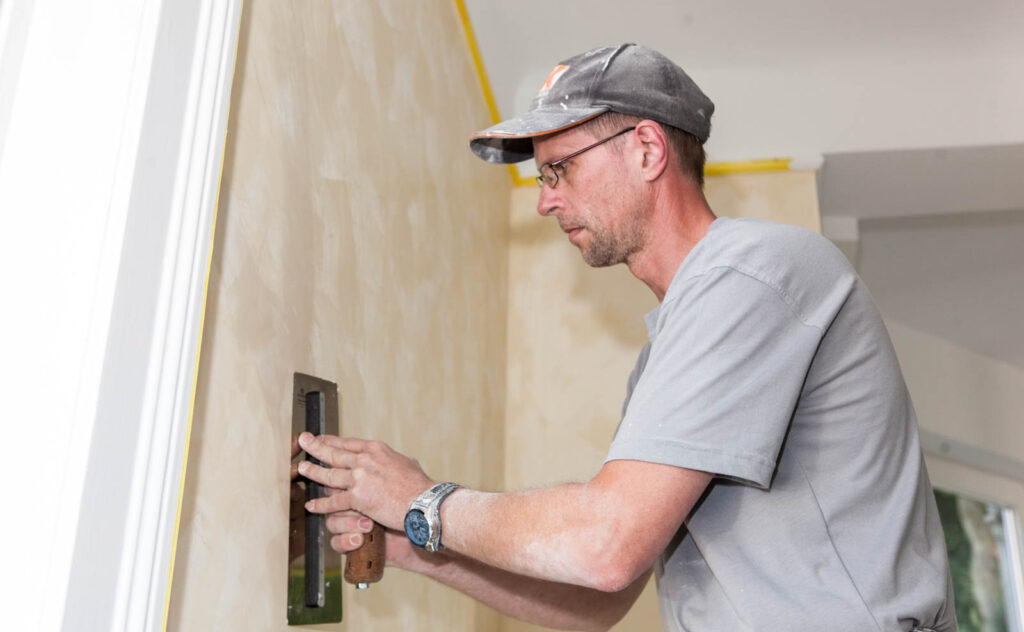 Malerarbeiten - Handwerker bearbeitet Wand mit Werkzeug.